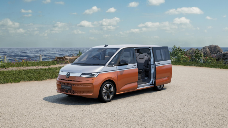 an orange and silver VW Multivan parked by a body of water
