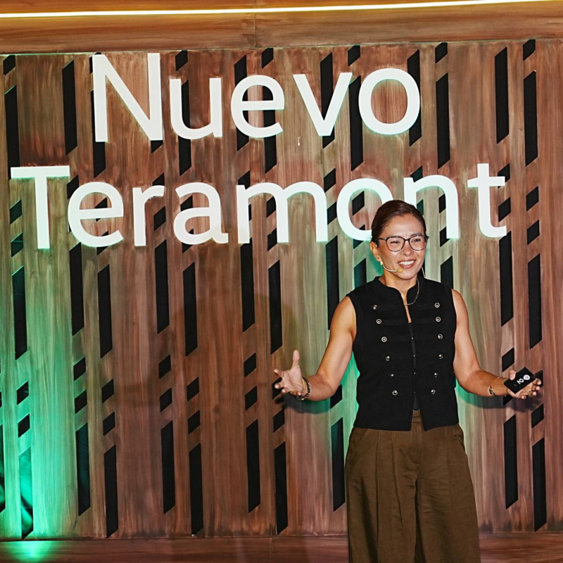 Directiva de Volkswagen con gafas y micrófono presenta Nuevo Teramont frente a un escenario de madera con luz verde.