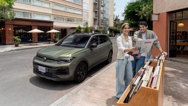 Volkswagen Taigun gris frente a una tienda; una pareja revisa discos en una caja de madera.