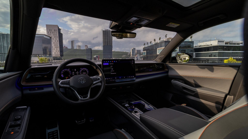 Interior de Volkswagen Teramont con volante, tablero digital, pantalla central, consola y acabados oscuros.