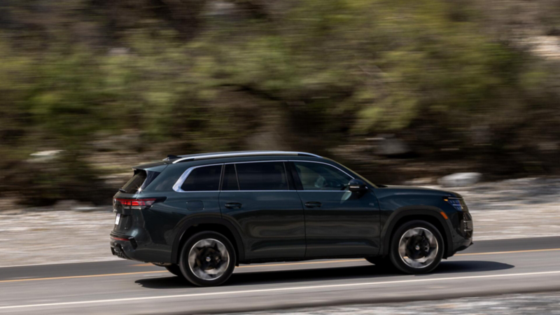Volkswagen Teramont oscuro de perfil sobre una carretera, con árboles y vegetación al fondo.