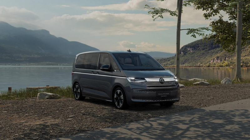 a grey Multivan parked by a lake with mountains in the background