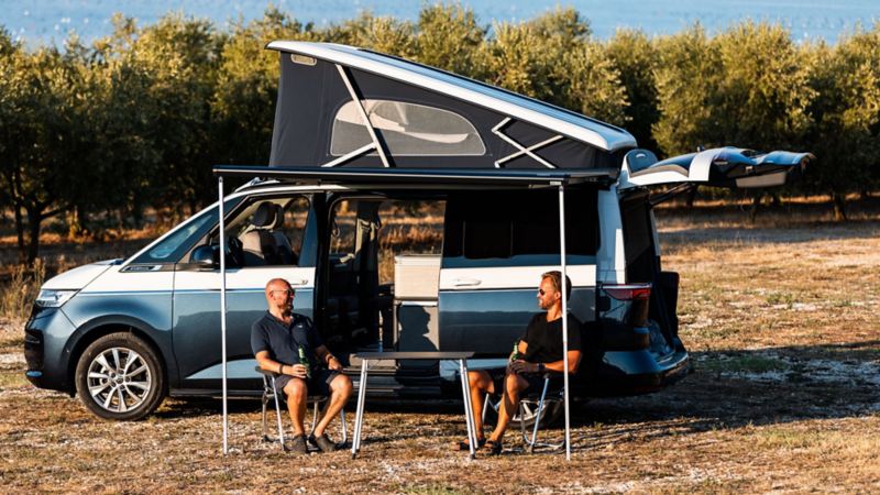 Två män sitter utanför en VW California campingbil med popup-tak