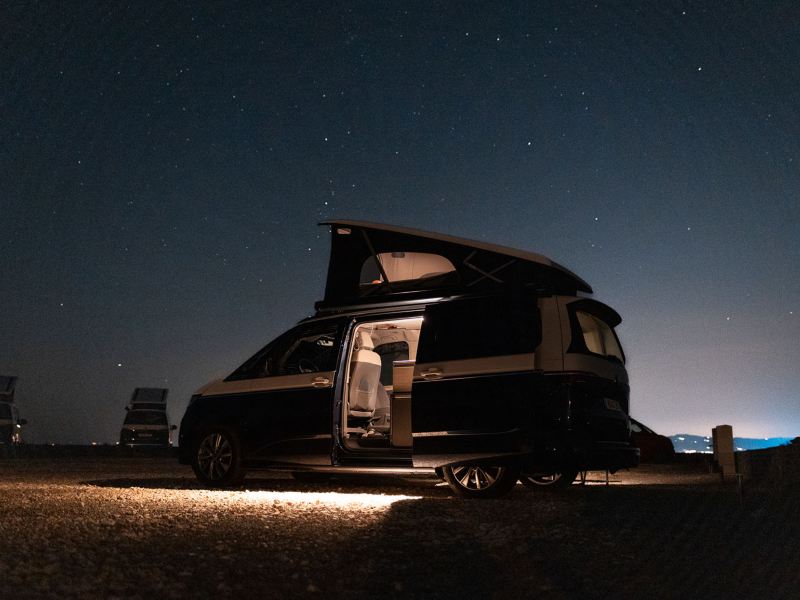 En VW California campingbil med uppfällt popup-tak under stjärnklar himmel