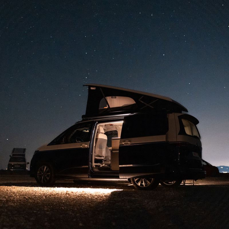 En VW California campingbil med uppfällt popup-tak under stjärnklar himmel