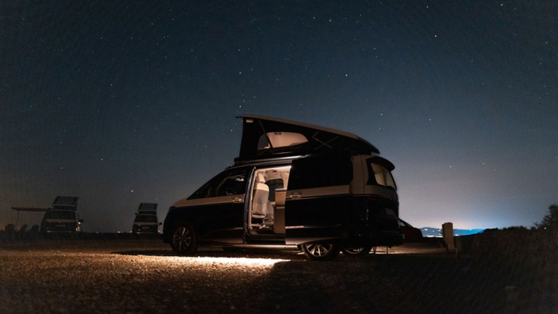 En VW California campingbil med uppfällt popup-tak under stjärnklar himmel