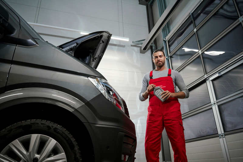 Pracownik serwisu stoi obok dostawczego Volkswagena z otwartą maską, trzymając w rękach butelkę jednego z płynów eksploatacyjnych.