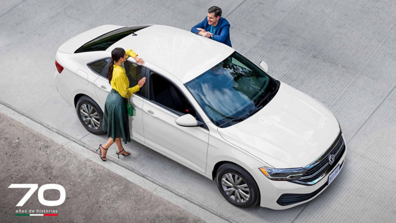 Auto sedán Jetta, edición 2024, en color blanco con pasajeros que platican sobre el carro. 