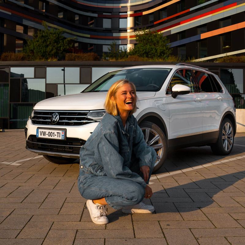 Une femme est accroupie devant un Tiguan eHybrid blanc.