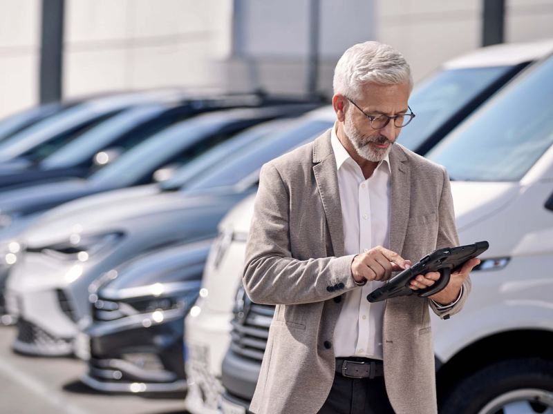 a man looking at an iPad while standing next to a fleet of VW vehicles