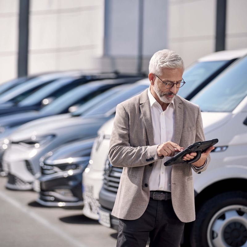 a man looking at an iPad while standing next to a fleet of VW vehicles