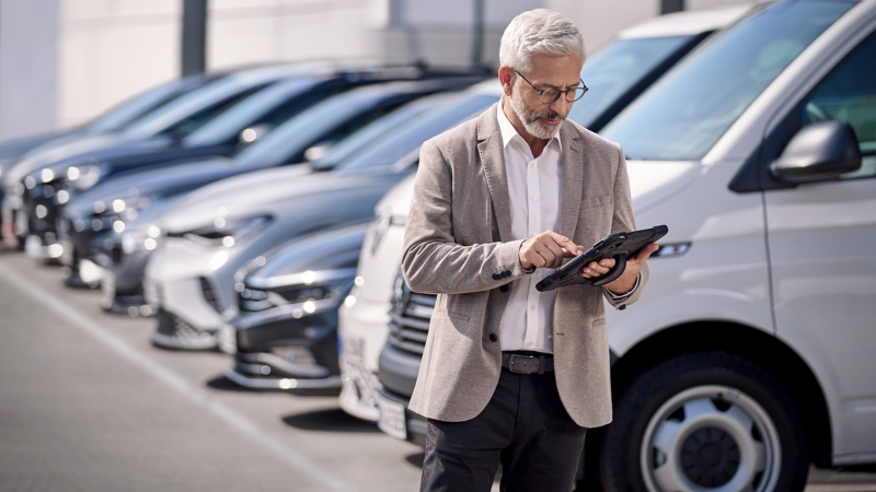 A man looking at an iPad while standing next to a fleet of VW vehicles. 