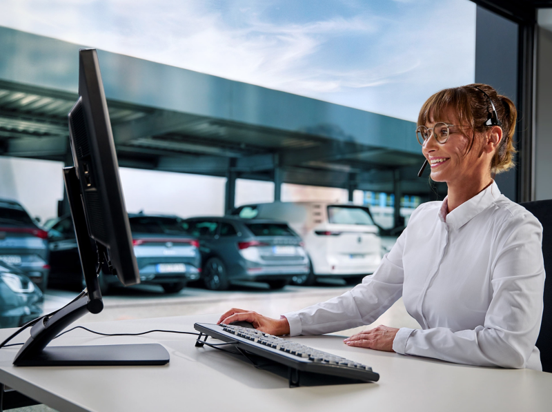 A fleet manager with a headset on with a fleet of cars in the window