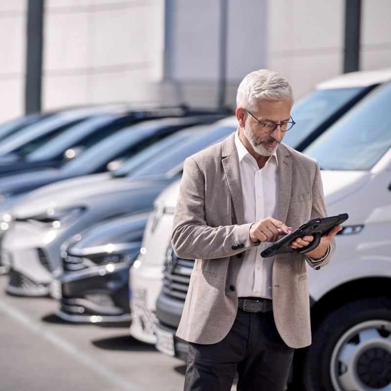 a man looking at an iPad while standing next to a fleet of VW vehicles