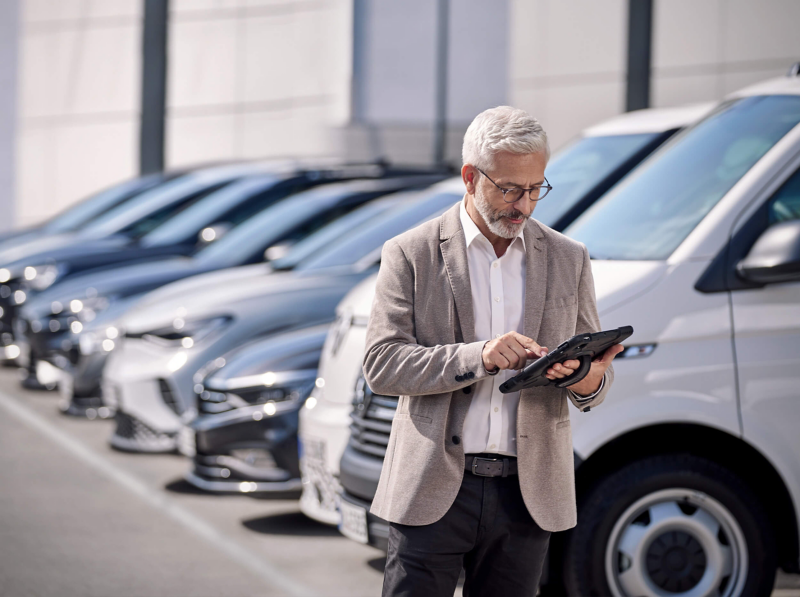 A man looking at an iPad while standing next to a fleet of VW vehicles. 