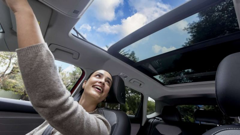 Mujer mira hacia el techo corredizo de un auto Volkswagen. 