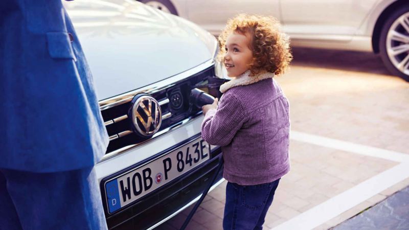 Una bambina inserisce il connettore per la ricarica nel cofano di un'auto ibrida plug-in Volkswagen