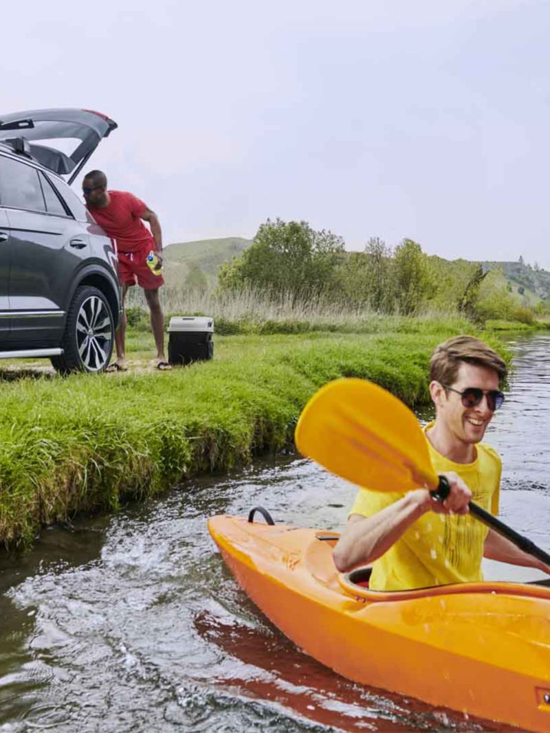 Il primo piano ragazzo che va su una canoa, dietro di lui un altro prende una borsa dal bagagliaio di una Volkswagen.