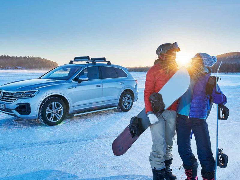 Una Volkswagen parcheggiata su un campo innevato con pneumatici invernali e una coppia di ragazzi vicino.