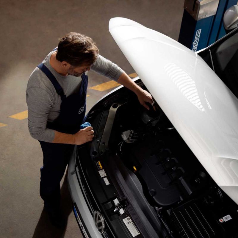 Un meccanico di Volkswagen Service ispeziona il motore di un'auto VW col cofano aperto.