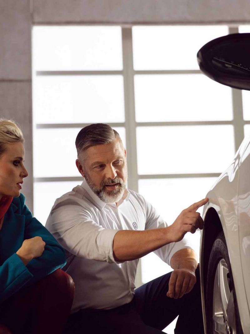 Un impiegato Volkswagen Service indica a una cliente la carozzeria dell'auto sopra allo pneumatico.