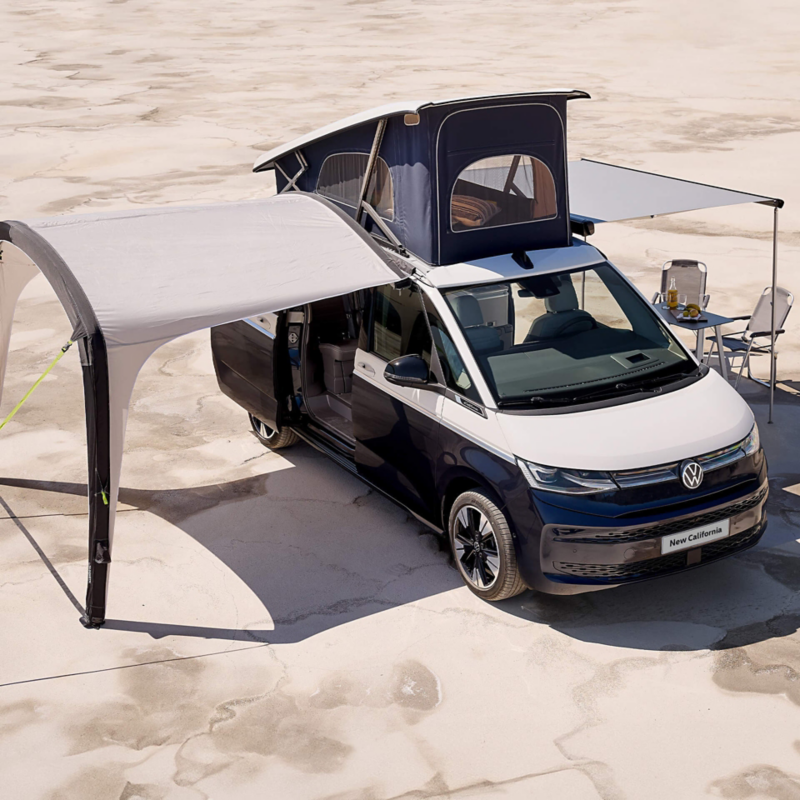 Photo of a VW California parked on a beach with its roof unit and awning deployed. 