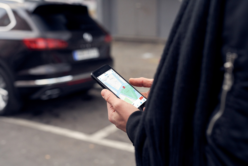A man holds his mobile phone, the screen displays the We Park app