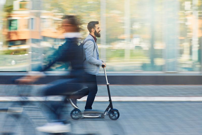 A man rides an electric scooter along the pavement passing a woman on a bike