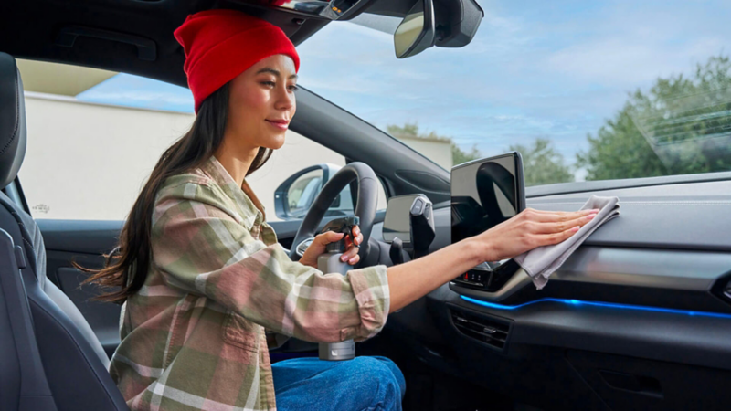 Une femme installée côté conducteur nettoie le tableau de bord d'une Volkswagen.