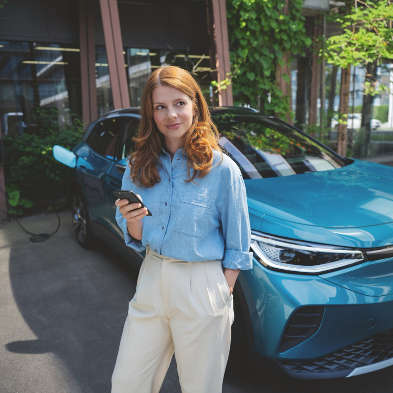 A woman standing in front of a Volkswagen ID.4 with a phone in her hand