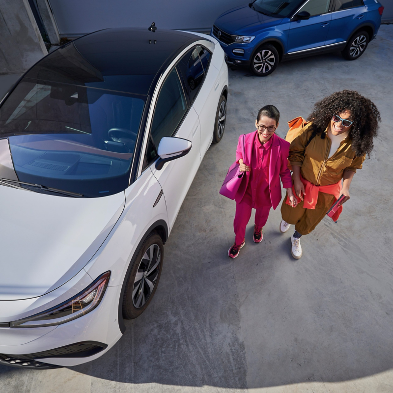 Two women talking next to a white and a blue Volkswagen ID.5