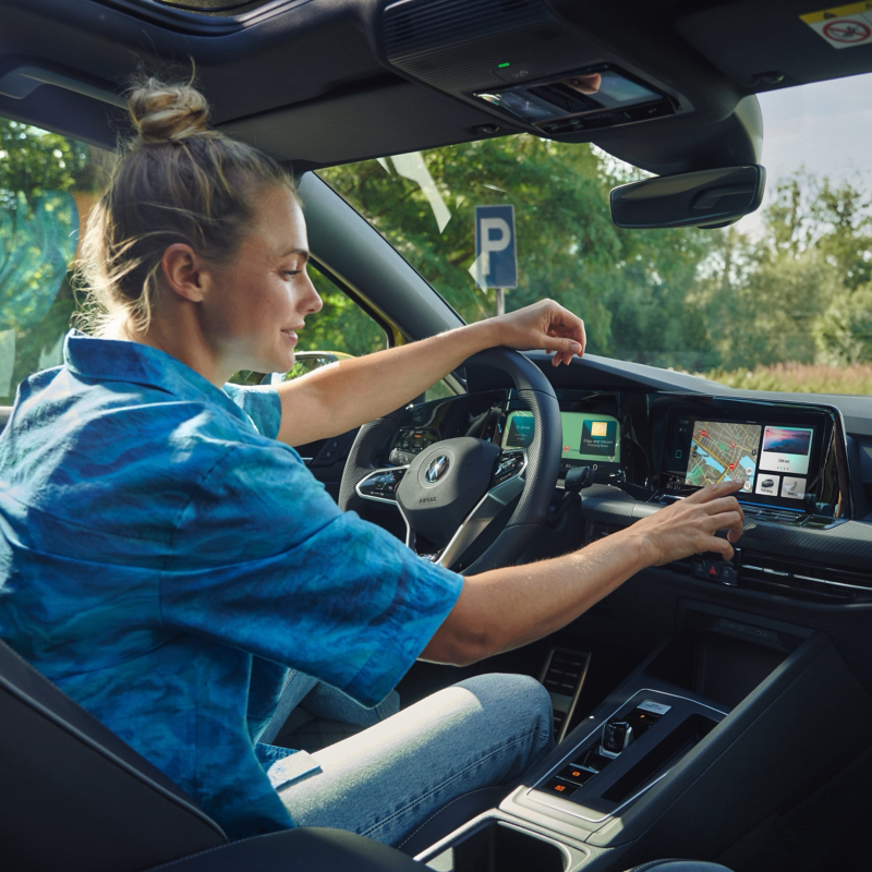 Woman sitting in a VW Golf, setting up the driving route - Vehicle import and export