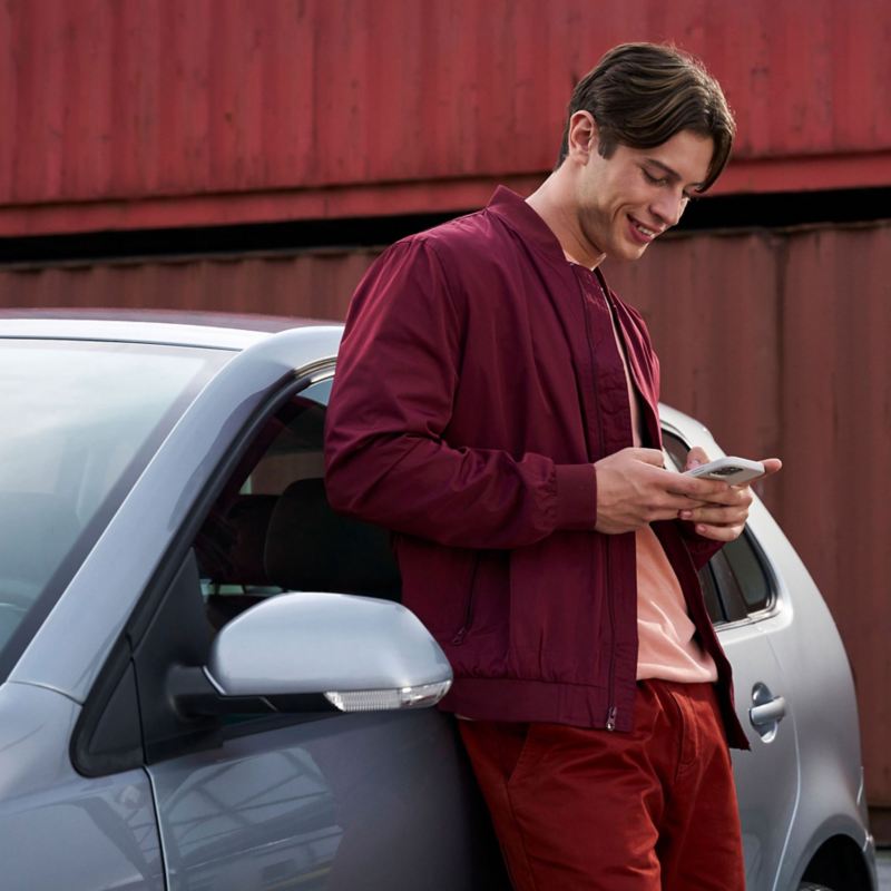 A man using a mobile phone and leaning on a VW car