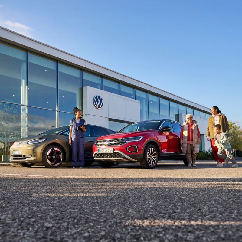 A family of 3 and a VW service employee standing around 2 Volkswagen cars