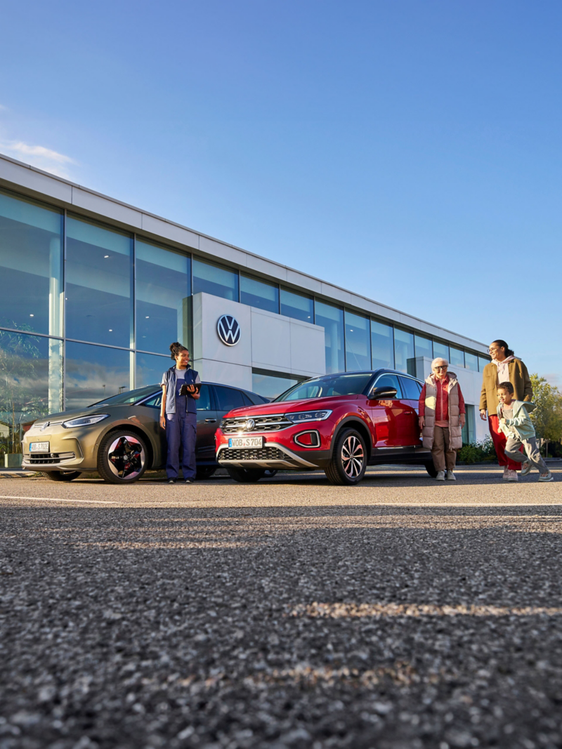 A family of 3 and a VW service employee standing around 2 Volkswagen cars