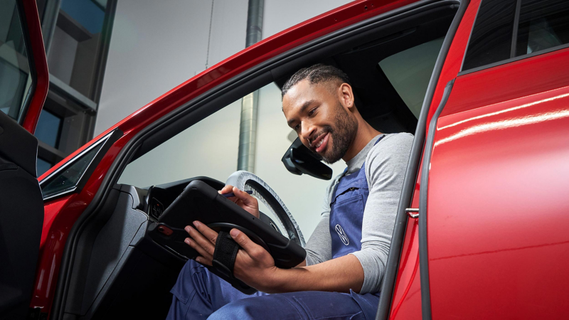 A VW service expert sitting partially inside a car with a tablet in his hand