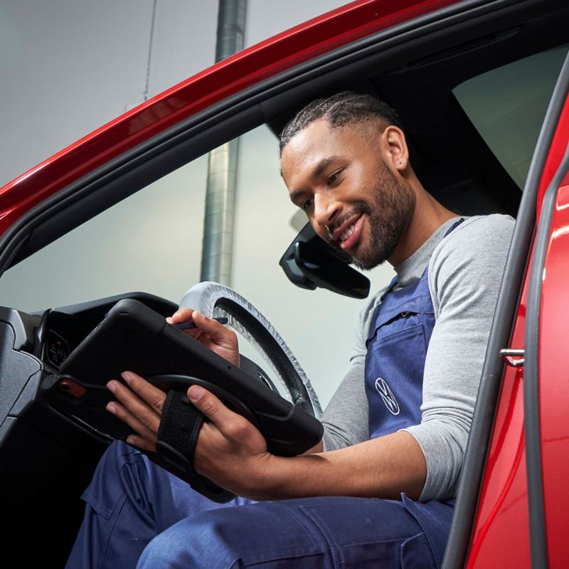 A VW service expert sitting partially inside a car with a tablet in his hand