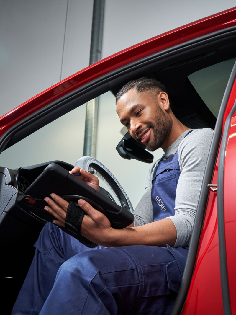 A VW service expert sitting partially inside a car with a tablet in his hand