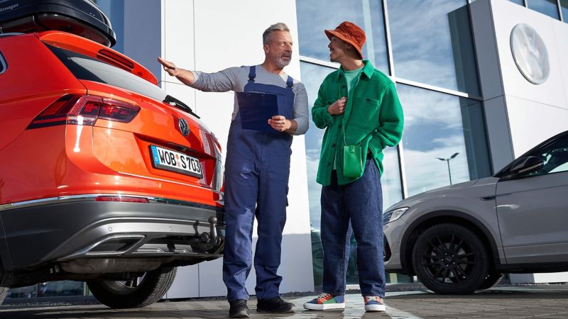 A VW service expert talking with a customer outside a service building