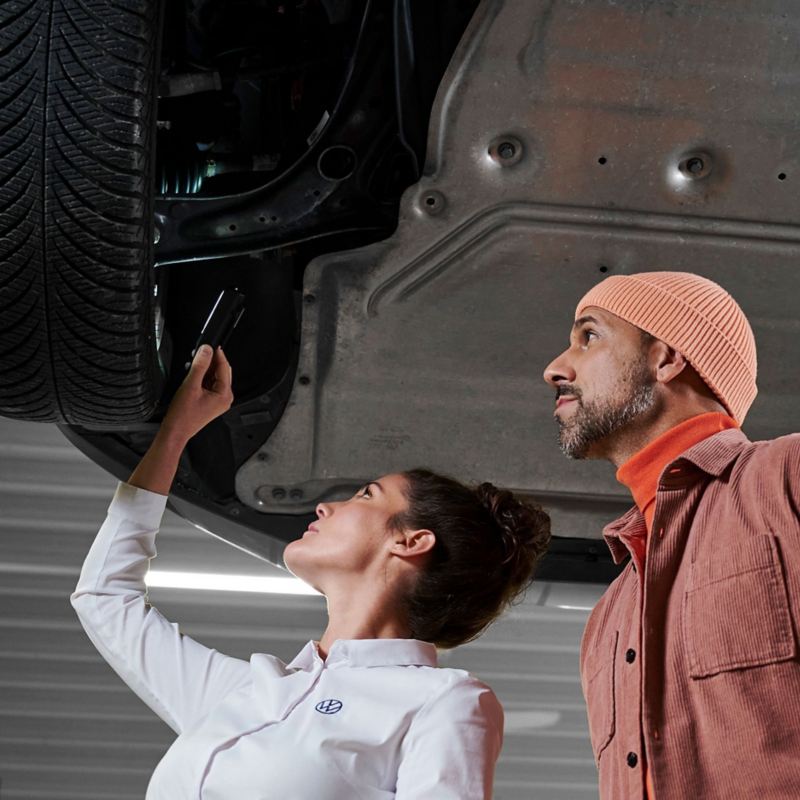 VW car on a lifting platform, VW service employee and customer look at the brakes together