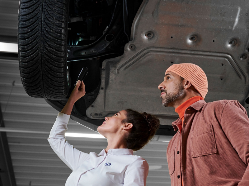 VW car on a lifting platform, VW service employee and customer look at the brakes together