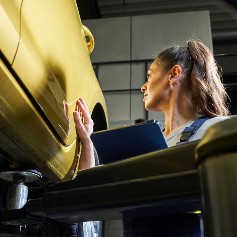 VW service employee with clipboard looks at the paintwork of a VW car