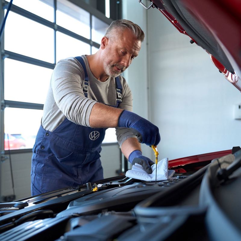 A VW service employee checking oil level within a car's bonnet