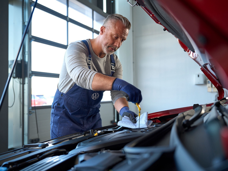 A VW service employee checking oil level within a car's bonnet