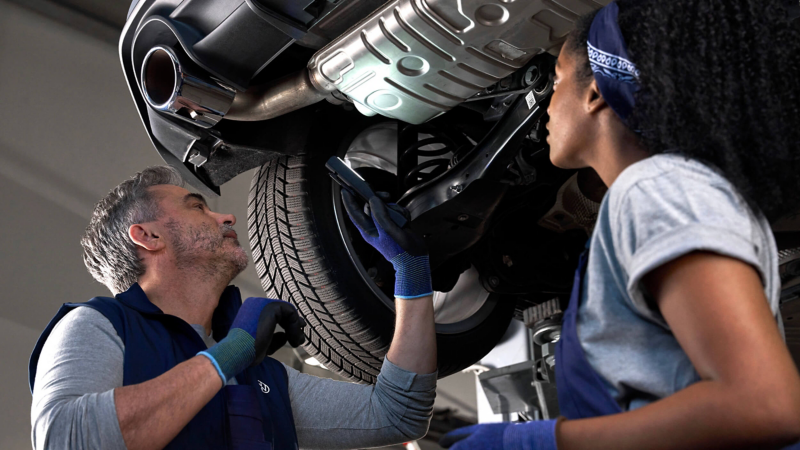 Two Volkswagen service experts inspecting the bottom of a car