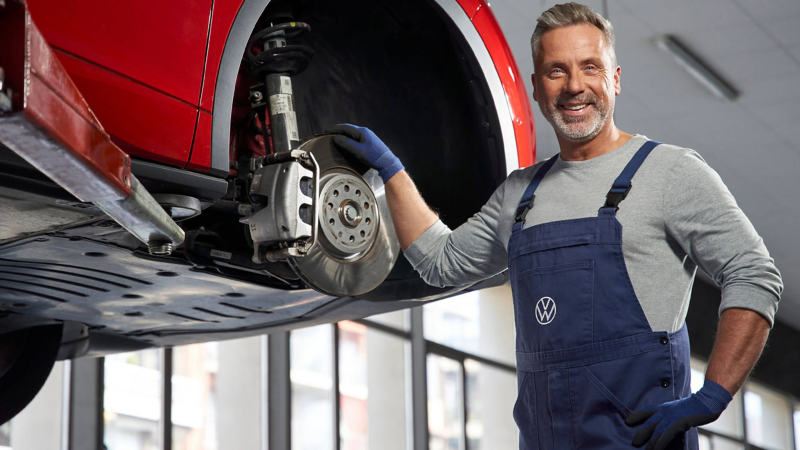 A VW service expert holding onto a brake pad of an elevated VW vehicle