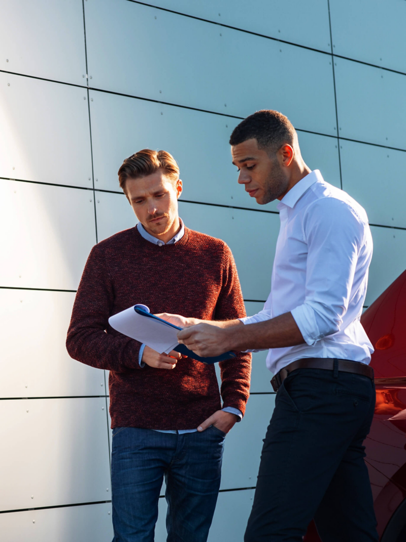 Two men looking at a chart next to a car