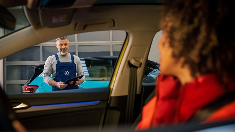 A VW service expert holding a tablet and smiling at a customer in her car