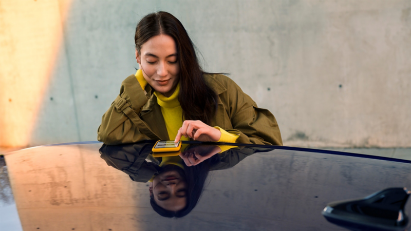 a woman looking at her phone whilst leaning on the roof of a VW