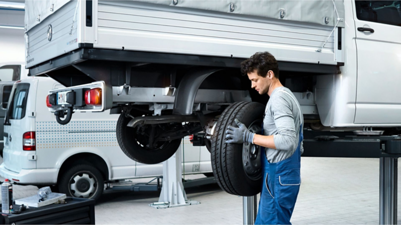 Volkswagen technician changing a tyre on a raised commercial vehicle in a workshop.